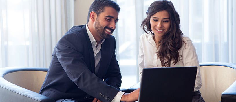 Man and woman smiling while looking at a laptop.